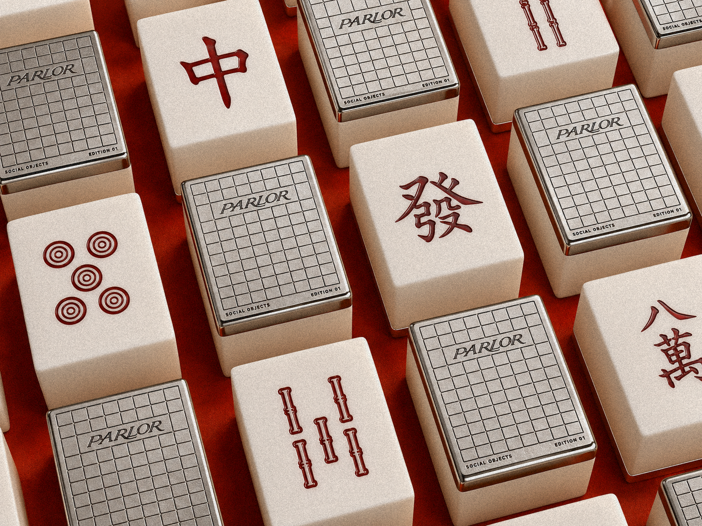 An array of PARLOR mahjong tiles on red felt, alternating face-up and face-down, showing the cream face with red ink-filled engraving and the brushed zinc back.